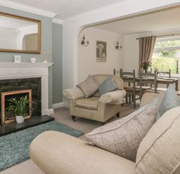A living room with beige sofas a fireplace with a mirror above and a dining table by a window at Humble Bee Cottage in Wold Newton near Hunmanby