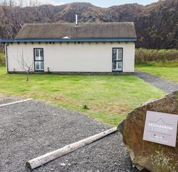A small lodge with two windows and a grassy yard surrounded by rocky hills at Restharrow Lodge Bamburgh