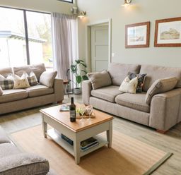 A living room with three sofas a coffee table and framed pictures on the wall at Restharrow Lodge in Bamburgh