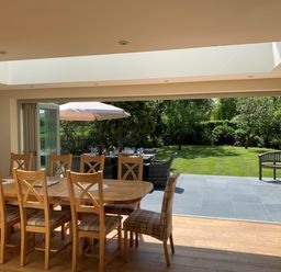 A dining area with wooden table and chairs opening to a garden with outdoor seating and umbrella at The Retreat in Lympsham