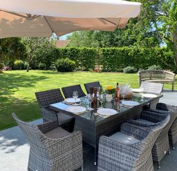 An outdoor patio with a dining table set with plates and glasses under a large umbrella at The Retreat in Lympsham
