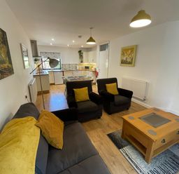 A living room with a sofa and armchairs around a coffee table next to an open kitchen with dining table at Stable Cottage in Shipham