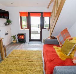 A living room with a grey sofa covered with cushions and a throw beside a wooden staircase at Bwlch Y Gwynt Bach in Llangefni