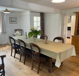 A dining room with a large table covered by a polka dot tablecloth six wooden chairs a wooden cabinet with plates and wine bottles and a vase with flowers on the table at Ribby Farmhouse in Lerryn
