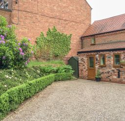 A brick cottage with a wooden door and windows next to a garden with hedges and flowering plants at Cream Door Cottage in Kidderminster