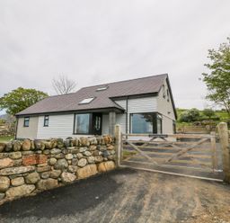 A house behind a wooden gate with stone walls and trees around at Llwyd Coed Canol in Llanllyfni near Penygroes