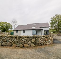 A house with a stone wall and wooden gate surrounded by trees at Llwyd Coed Canol in Llanllyfni near Penygroes