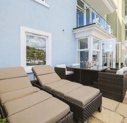 An outdoor patio with two lounge chairs and a dining table set with chairs at Quayside Dart Marina in Dartmouth