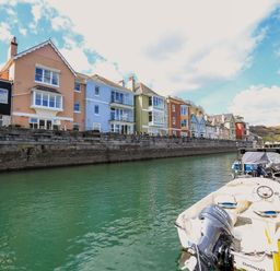 A row of colorful houses along a waterfront with boats docked at a marina at Quayside Dart Marina in Dartmouth