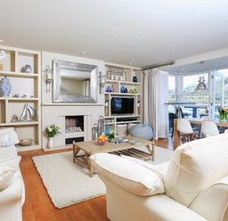 A living room with cream sofas a wooden coffee table a fireplace built in shelves and dining area with large windows at Quayside Dart Marina in Dartmouth