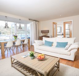 A living room with a white sofa blue cushions a wooden coffee table and a dining table with white chairs and pendant lights at Quayside Dart Marina in Dartmouth