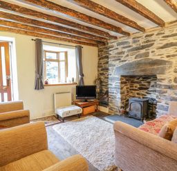A living room with two armchairs a sofa a small television on a table a stone fireplace and wooden ceiling beams at Dyfi Cottage in Dolgellau
