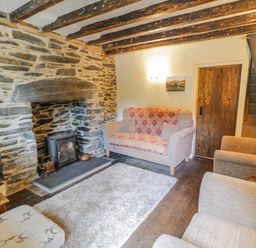 A living room with a stone fireplace wooden beams on the ceiling a sofa armchairs a rug and a wooden door at Dyfi Cottage in Dolgellau