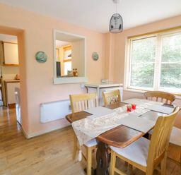 A dining room with a wooden table and six chairs near a window with blinds at Dyfi Cottage in Dolgellau