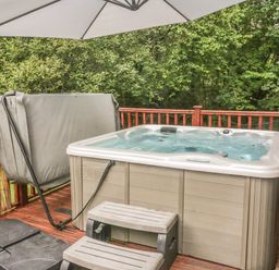 A hot tub with steps and a patio umbrella on a wooden deck surrounded by trees at 40 Skiptory Howe in Troutbeck Bridge