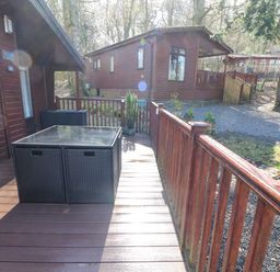 A wooden deck with a glass top table and two black chairs outside a wooden cabin at 40 Skiptory Howe in Troutbeck Bridge