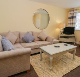 A living room with a beige sofa, coffee table, armchair, television on a stand and window at Valiant House in Scarborough
