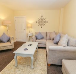A living room with a beige armchair and a corner sofa with cushions a white coffee table and two lamps at Valiant House in Scarborough