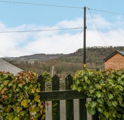 A wooden gate covered with ivy overlooking a rural landscape with hills under a blue sky at Tudor House in Symonds Yat