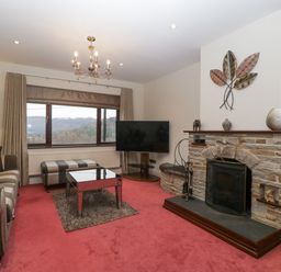 A living room with a striped sofa ottoman glass coffee table stone fireplace and television at Tudor House in Symonds Yat