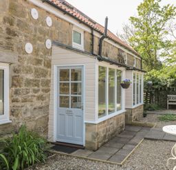 Stone building with a light blue door labeled Robin and large windows with hanging flower baskets and a garden bench at Robin Cottage in Morpeth