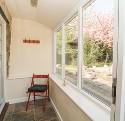 A small enclosed porch with a red chair and stone floor looking out to a garden with pink flowering tree at Robin Cottage in Morpeth