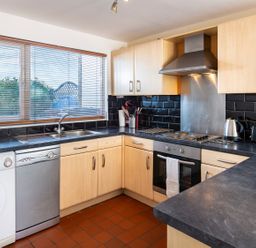 A kitchen with wooden cabinets black countertops a washing machine dishwasher stove oven kettle toaster and a window at 164 Cumber Close in Malborough