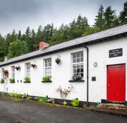 A white building with red doors and flower pots on windowsills surrounded by trees at The Old School in Gortin