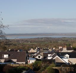A hillside view of rooftops with a river and fields in the background at Isallt in Rhostryfan near Bontnewydd Gwynedd