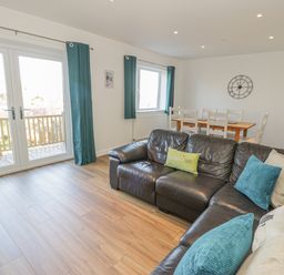 A living room with a black leather sofa blue curtains and a wooden dining table at Isallt in Rhostryfan near Bontnewydd Gwynedd