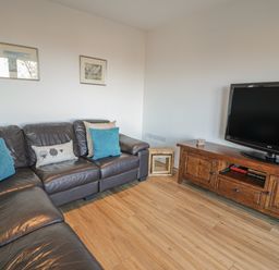 A living room with a brown leather sofa and wooden TV stand with a flat screen TV at Isallt in Rhostryfan near Bontnewydd Gwynedd
