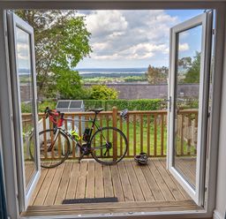 A balcony with a bike and a helmet looking out to a garden and distant landscape at Isallt in Rhostryfan near Bontnewydd Gwynedd