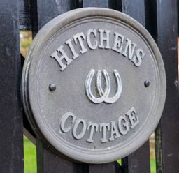A round metal sign with horseshoes and the text Hitchens Cottage on a black wooden fence at Hitchens Cottage in Happisburgh