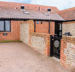Exterior view of a brick and flint cottage with a tiled roof a small black gate and a parking area at Hitchens Cottage in Happisburgh