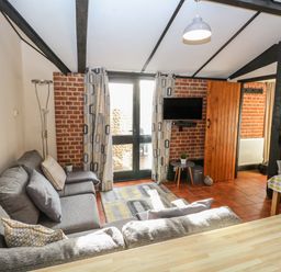 A living room with a grey sofa a wall clock and a small wall mounted television at Hitchens Cottage in Happisburgh