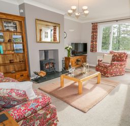 A living room with floral armchairs a wood stove bookcase and a television at Kirkstone Cottage in Outgate near Hawkshead