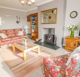 A living room with a patterned sofa and armchair a wooden coffee table a fireplace a wooden bookshelf and a television at Kirkstone Cottage in Outgate near Hawkshead