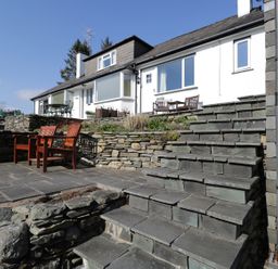 An outdoor patio with stone steps and wooden chairs in front of a white house at Kirkstone Cottage in Outgate near Hawkshead