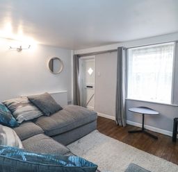A living room with a gray sectional sofa gray curtains a small black table a wall-mounted light and a window at Fenders in Brewers Quay Harbour