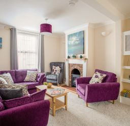 A living room with purple sofas and armchair a fireplace and wooden coffee table at Wey Cottage in Weymouth