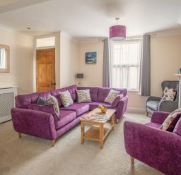 A living room with purple sofas a wooden coffee table a grey armchair and a window at Wey Cottage in Weymouth