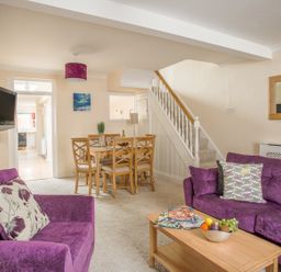 A living room with purple sofas a wooden dining table with chairs and a staircase at Wey Cottage in Weymouth