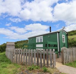 A small green wooden cabin with a fenced yard and chairs on a patio under a partly cloudy sky at Lady Bird Retreat in Skinningrove