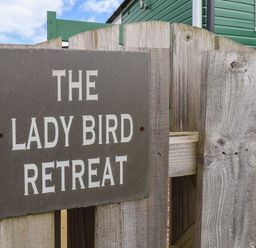 A wooden gate with a sign saying The Lady Bird Retreat and part of a green house visible in Skinningrove
