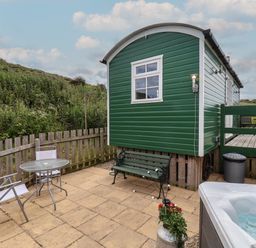 An outdoor patio with a green bench table and chairs a green wooden cabin a hot tub and a fence at Lady Bird Retreat in Skinningrove