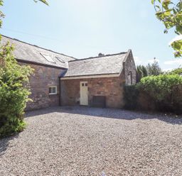 A gravel driveway in front of a stone building with a sloped roof and white door surrounded by bushes at The Coach House in Lowick near Holy Island