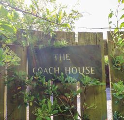 A wooden fence with a sign that says The Coach House surrounded by green plants at The Coach House in Lowick near Holy Island