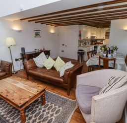 A living room with brown leather sofas a wooden coffee table a round upholstered chair and a dining table with chairs at The Coach House in Lowick near Holy Island