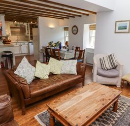A living room with a wooden coffee table a brown leather sofa and a armchair next to a dining table and kitchen at The Coach House in Lowick near Holy Island