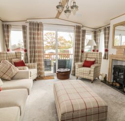 A living room with plaid armchairs sofa matching ottoman and curtains a fireplace and a sliding glass door at 27 Lake View in Cawston